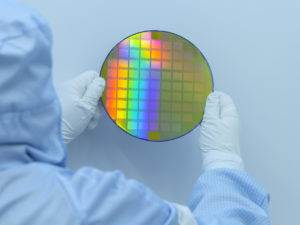 Engineer in clear room in white gloves and suit holding a silicon wafer with integrated circuits on a white background.